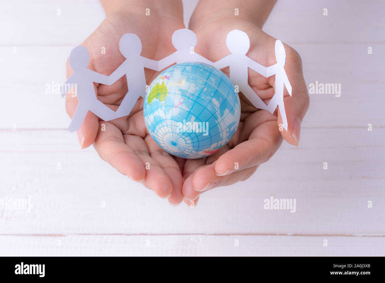 Closeup woman hands holding globe with white people chain made from paper cut. World population day. Stock Photo