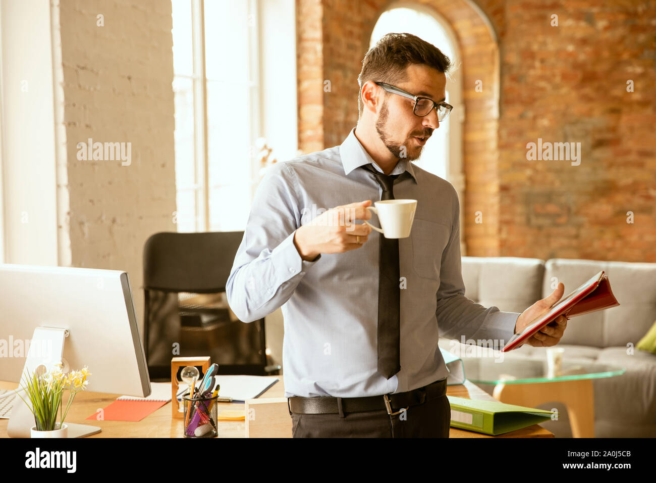 Deals. A young businessman working in the office, getting new work place. Young male office worker while managing after promotion. Looks confident. Business, lifestyle, new life concept. Drinks coffee. Stock Photo
