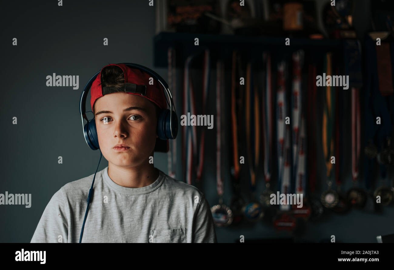 Tween boy wearing headphones standing in front of sports medals. Stock Photo