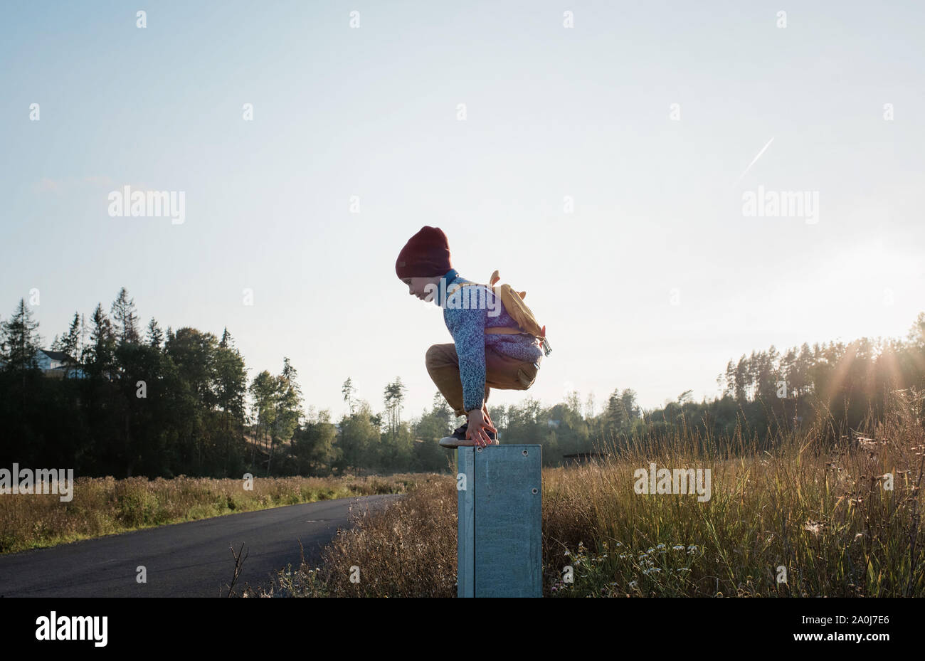 young school boy jumping off a post whilst walking home at sunset Stock Photo