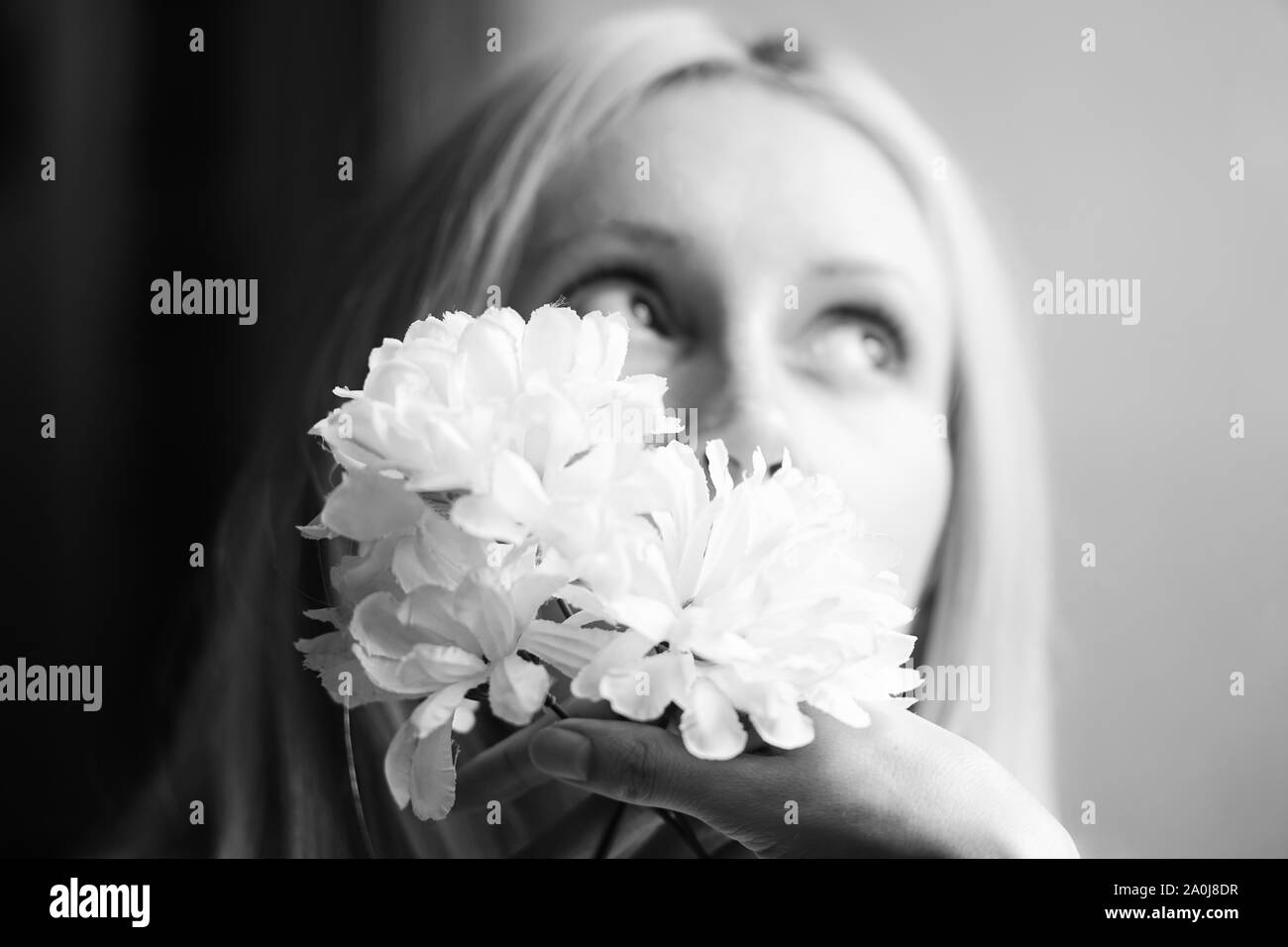 Blurred portrait of a young girl with flowers in hand, female dreams and pleasure. Selective soft focus. Black and white Stock Photo