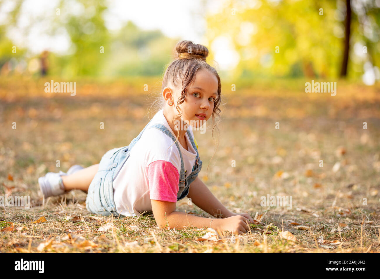 A front portrait of a little girl lying on a colorful leaves in autumn park Stock Photo