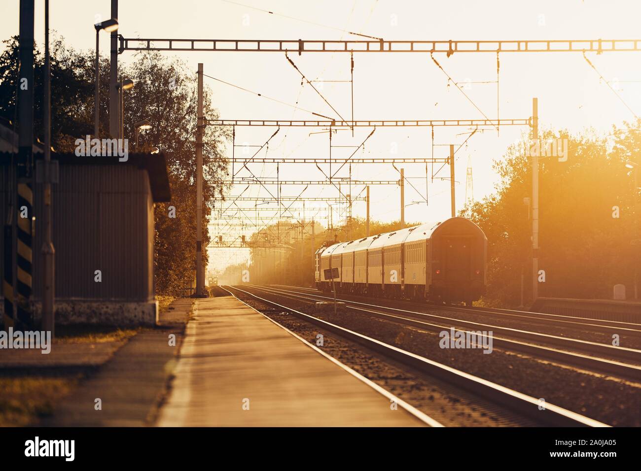 Railway at sunrise. Passenger train leaving from railroad station. Stock Photo