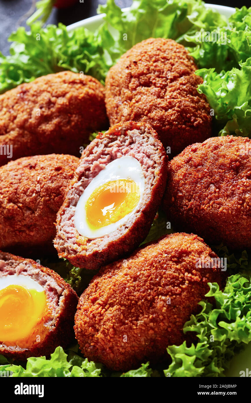 close-up of scotch eggs, boiled eggs wrapped in minced meat and deep fried, served with lettuce leaves on a plate, macro Stock Photo