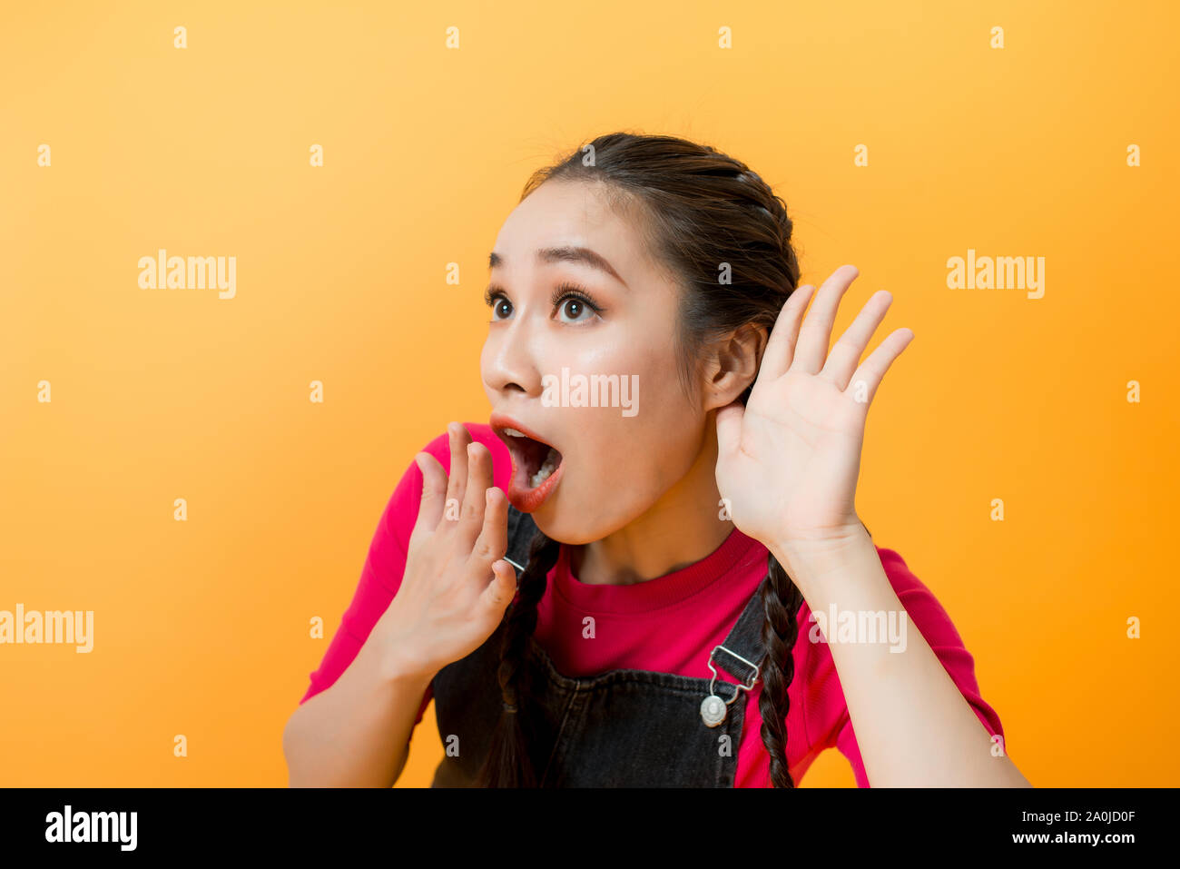 Young teenager Asian girl over isolated yellow background listening gossip by putting hand on the ear Stock Photo