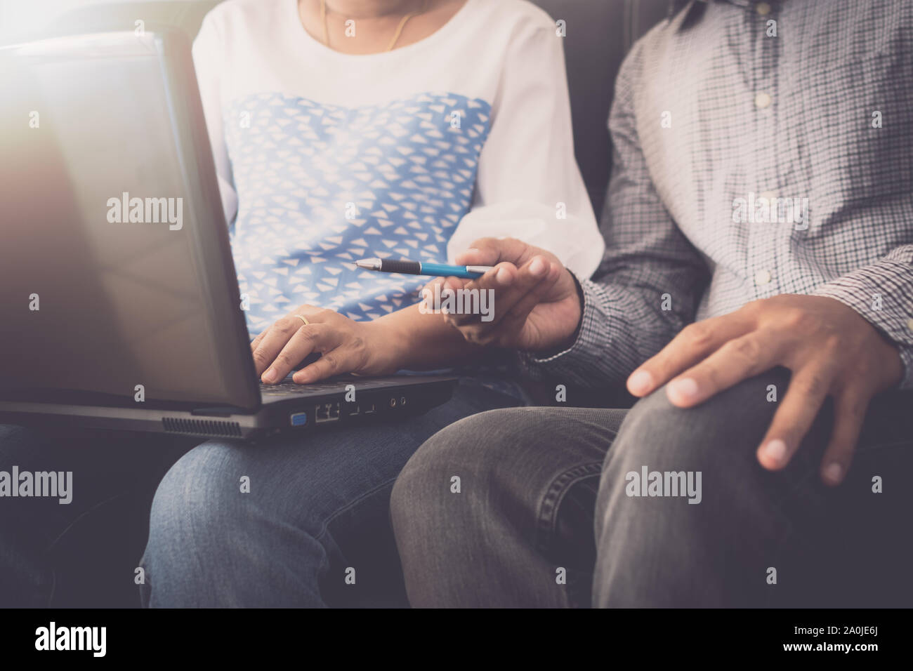 Man and woman workmate in casual dress discussing together while using laptop and sitting on sofa in office. Stock Photo