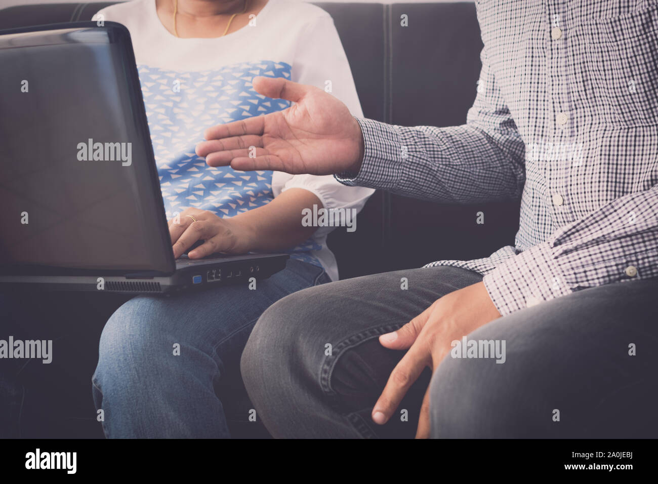 Man and woman workmate in casual dress discussing together while using laptop and sitting on sofa in office. Stock Photo