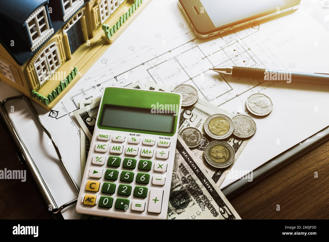 Investment for construction with limit budget, Construction plan, pen, money, model house, smart phone  and calculator on wooden table under light Stock Photo
