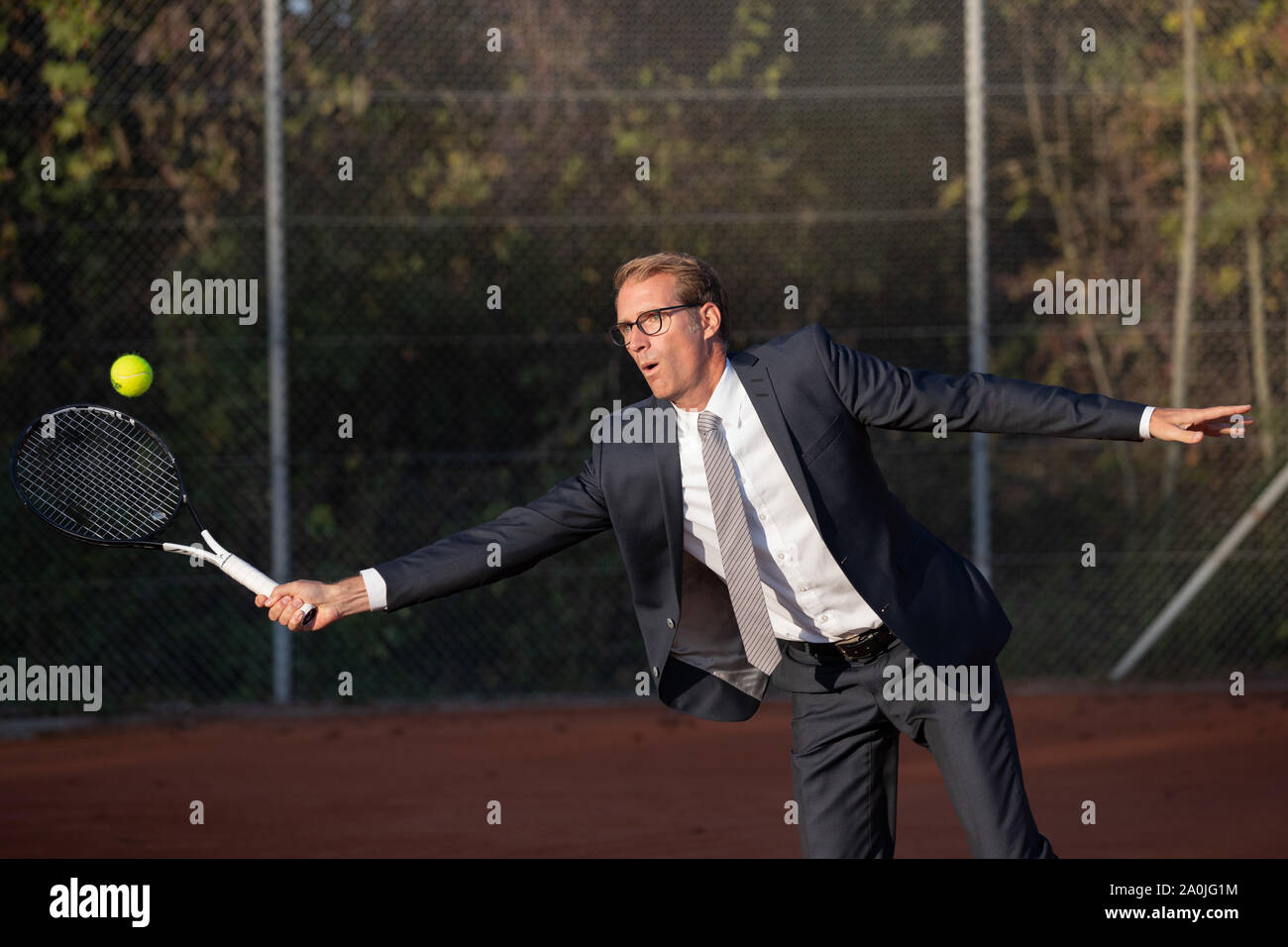 Smiling businessman in dark suit playing tennis Stock Photo