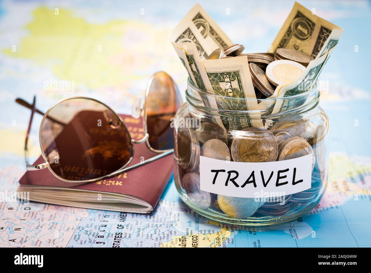 Travel budget concept. Travel money savings in a glass jar with passport and sunglasses on world map Stock Photo
