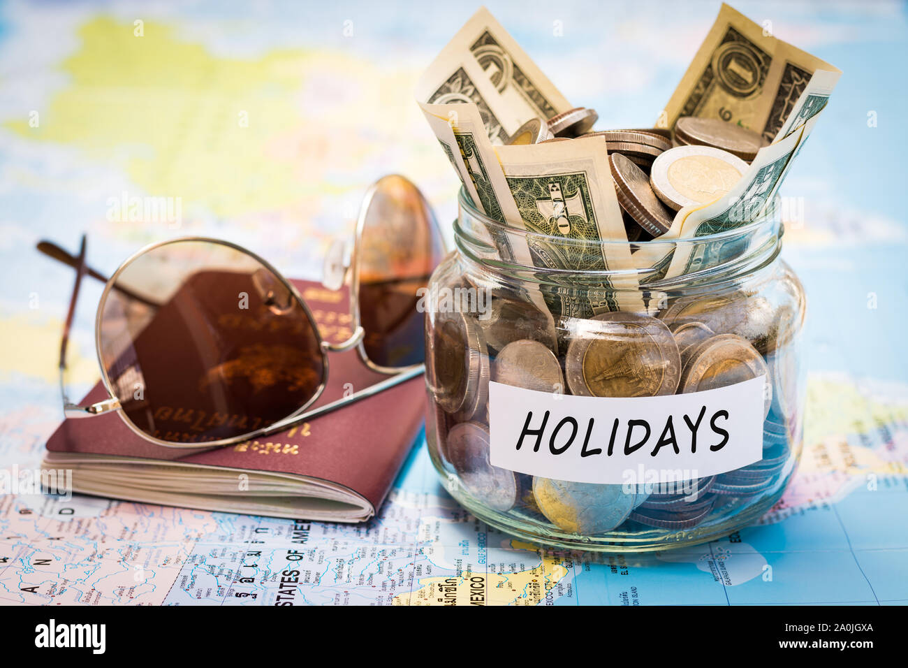 Holidays budget concept. Holidays money savings in a glass jar with passport and sunglasses on world map Stock Photo