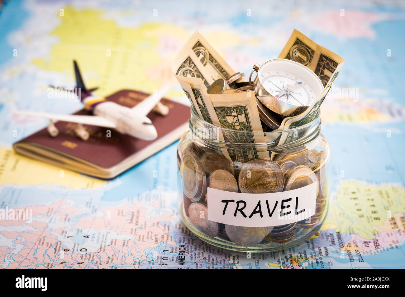 Travel budget concept. Travel money savings in a glass jar with compass, passport and aircraft toy on world map Stock Photo