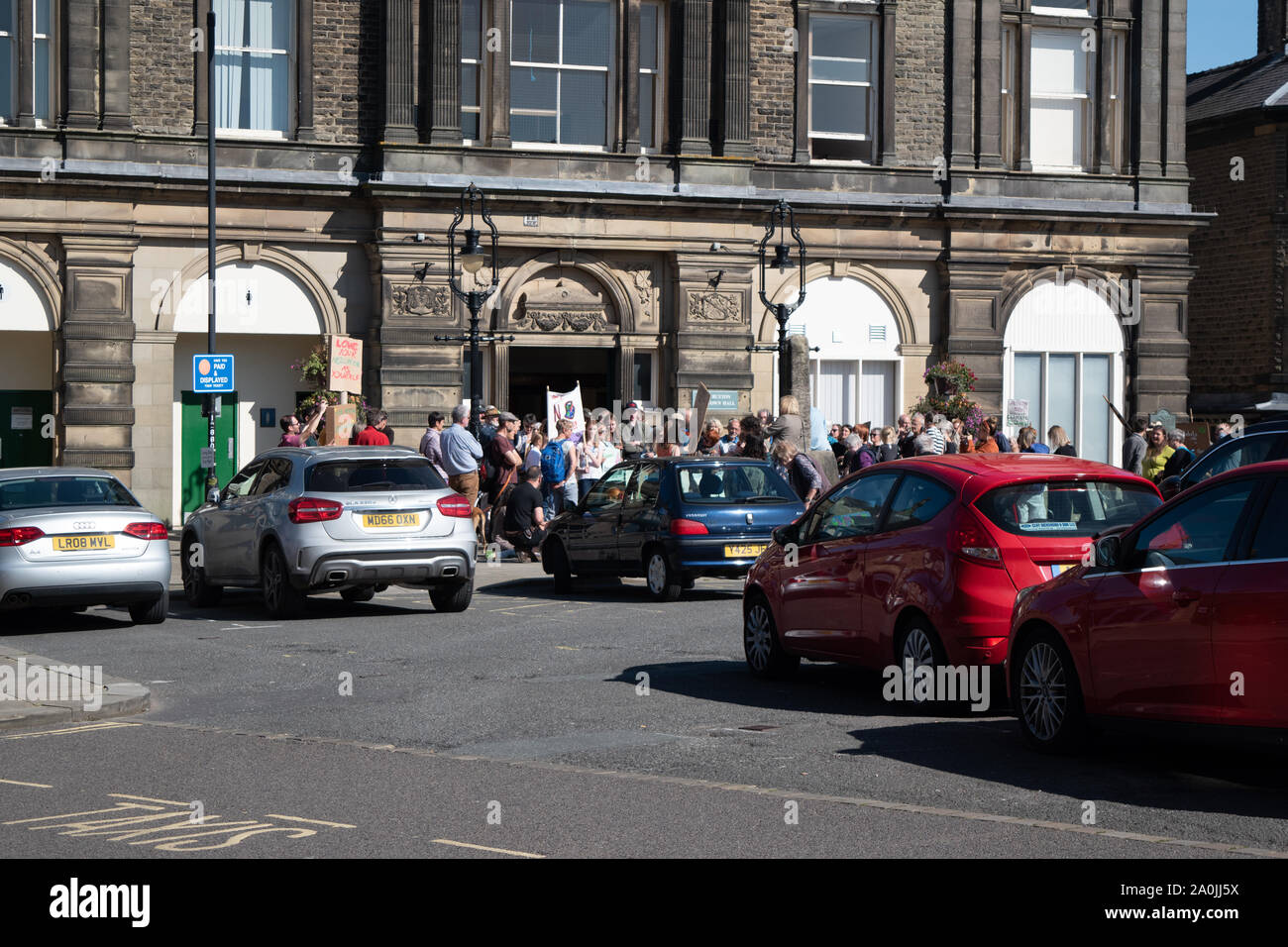 A small group of climate change demonstrators stood outside the local town hall in front of a car park full of cars in the small Peak District town of Stock Photo