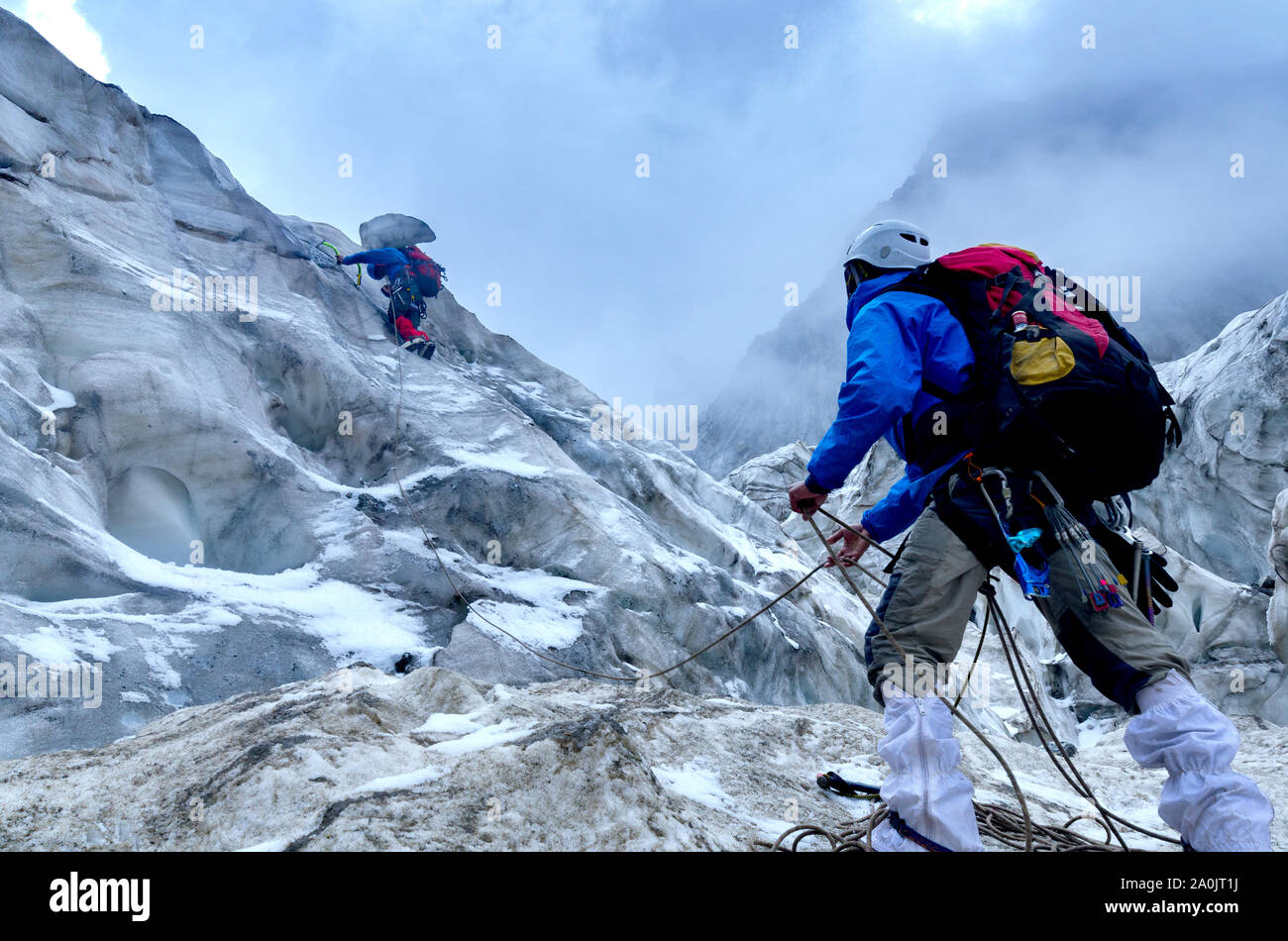 Two climbers are climbing the ice wall into the cloudy weather. Stock Photo