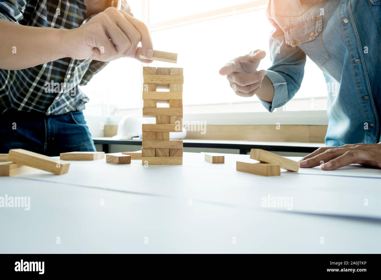 Hand of engineer playing a blocks wood tower game (jenga) on blueprint or architectural project Stock Photo