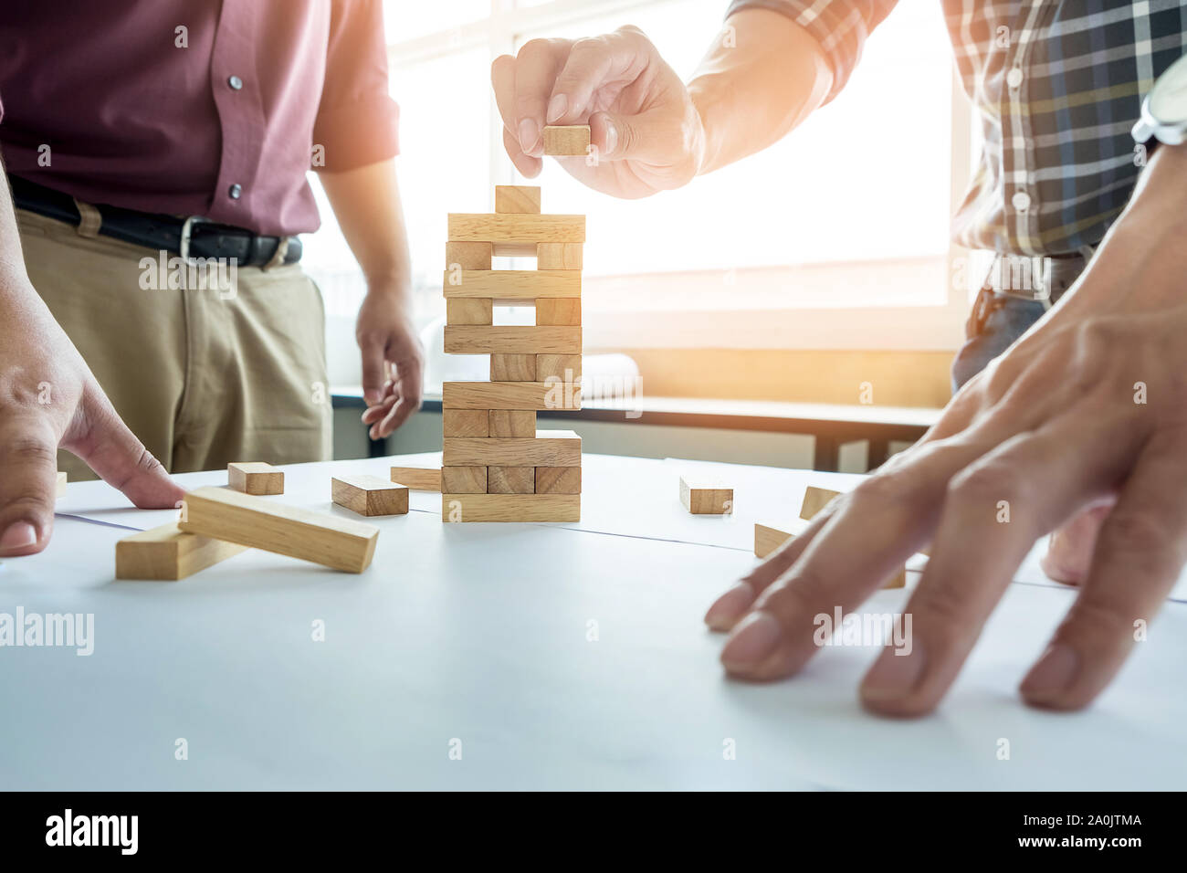 Hand of engineer playing a blocks wood tower game (jenga) on blueprint or architectural project Stock Photo