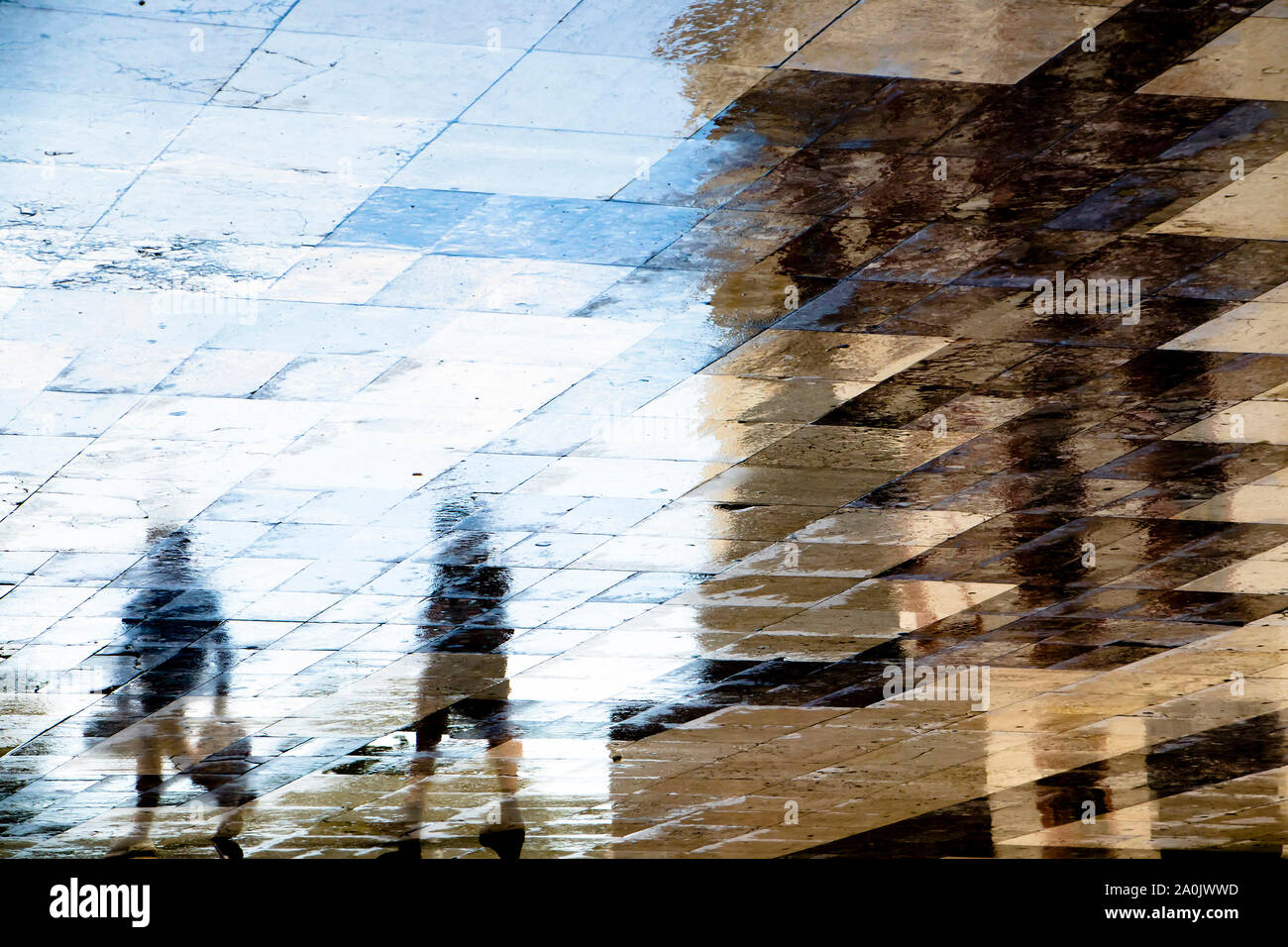 Blurry abstract shadow silhouette reflections of two people walking  on wet city street pavement Stock Photo