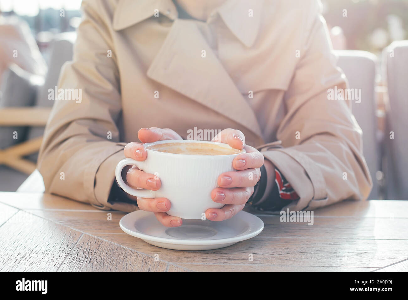 Big white coffee cup in woman's hands with pastel manicure while sitting in cafe. Stock Photo