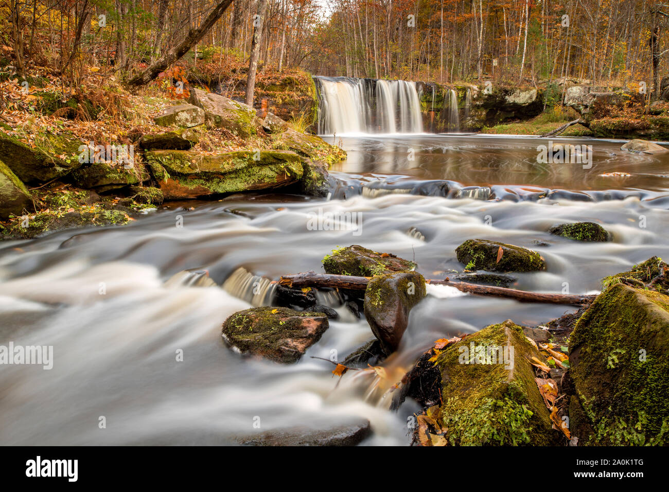 Silky smooth water flows over rapids downstream of Wolf Creek Falls in autumn. Stock Photo