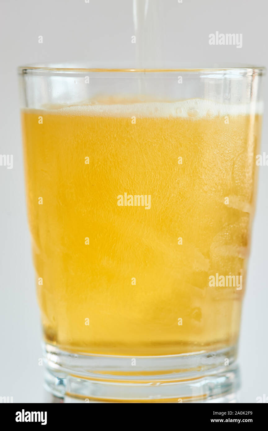 Photograph of a glass tumbler with its reflection in which a cold beer is falling, on a white background. Stock Photo