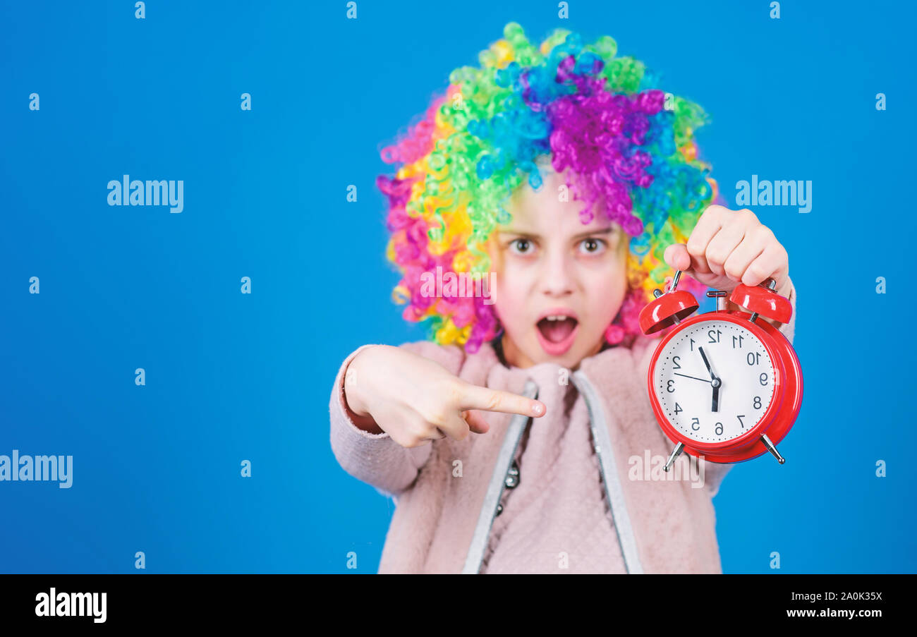 The clock ticking away the time. Adorable small child with colorful wig