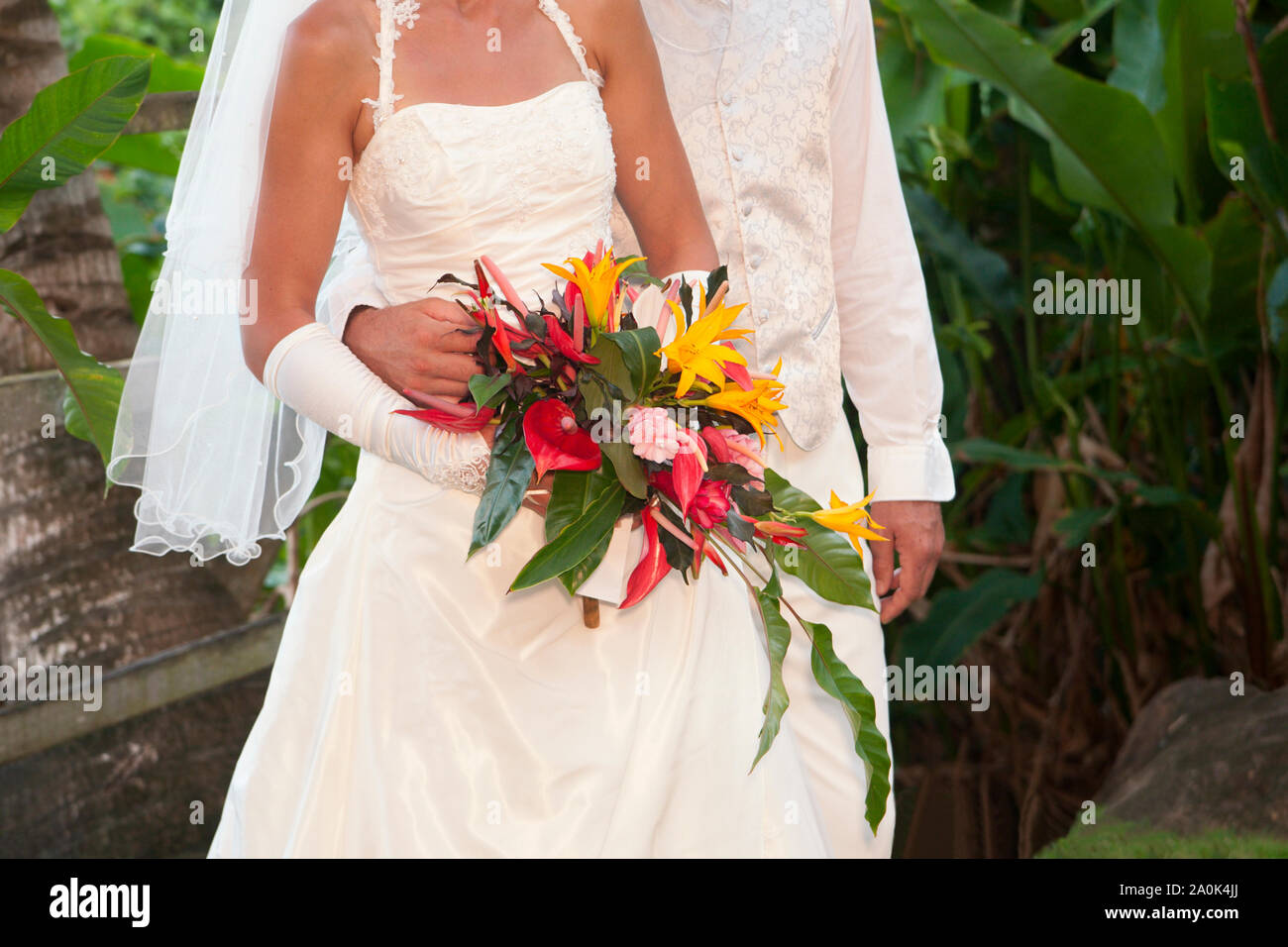 Partial view of a French couple wearing traditional white formal wedding attire holding native flowers during their wedding service outdoors in Domini Stock Photo