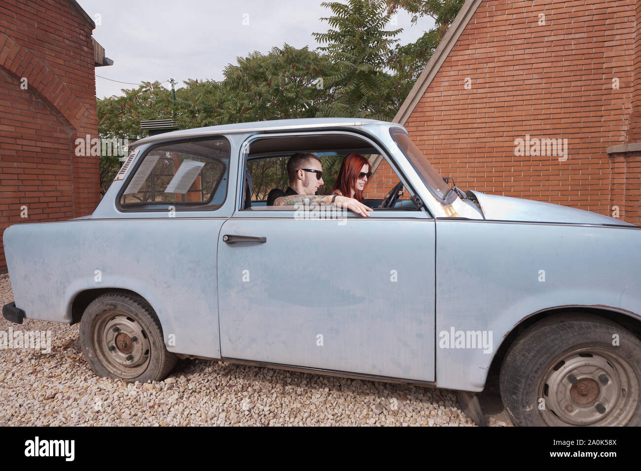 Red-haired woman and her tatooed boyfriend in his 20's sit inside a Trabant car that was popular during Communist time (typically had to wait 3 years Stock Photo