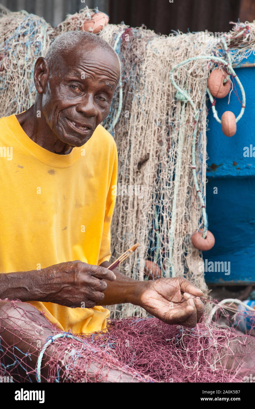 Senior aged balding man is repairing his fishing net, Scotts Head, Dominica, West French Indies, Caribbean, Central America Stock Photo