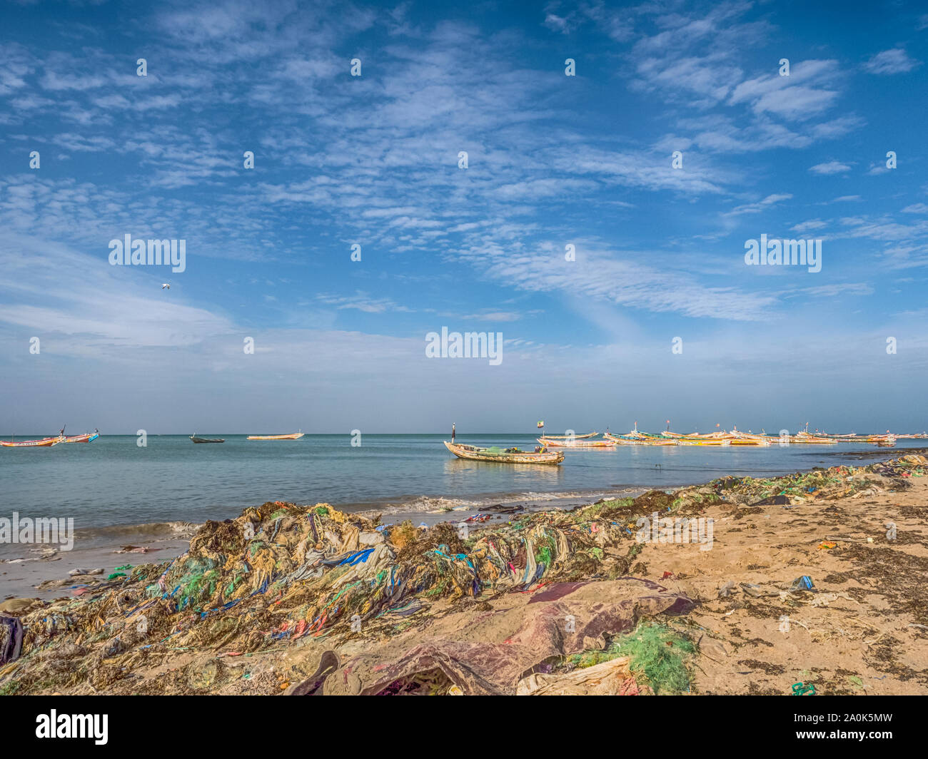 Senegal, Africa - January 26, 2019: Plenty of plastic bags on shore of the ocean. Pollution concept. Colorful fisher boats in the background. Senegal. Stock Photo