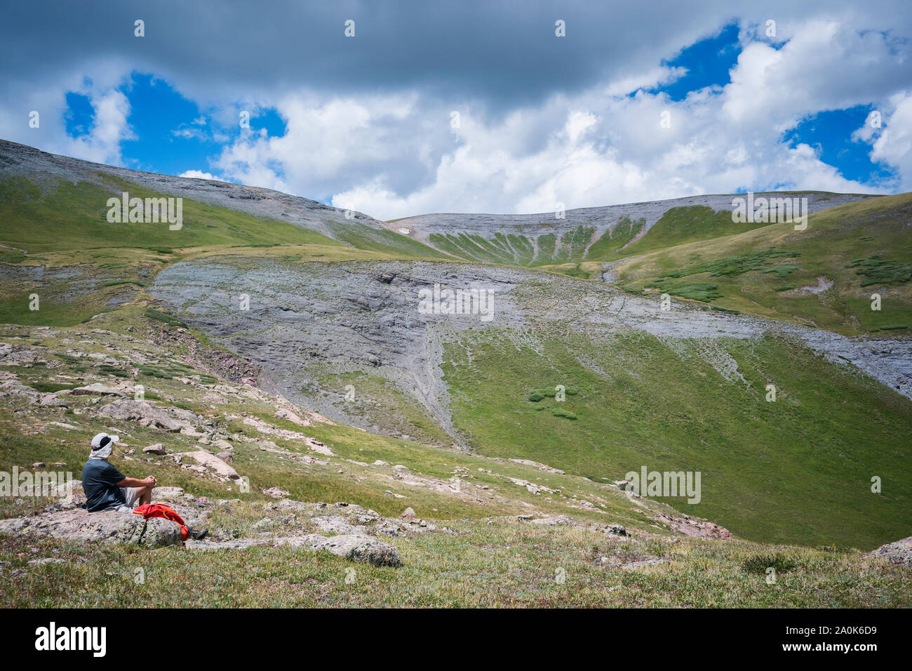 Senior adult man sits on a rock to take a rest break while hiking above tree line in the San Juan Mountains on a cloudy summer day, Weminuche Wilderne Stock Photo