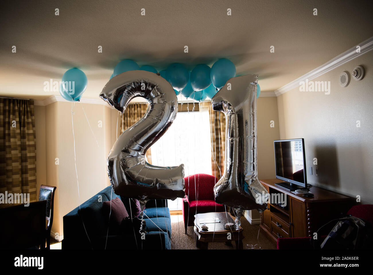 Shiny silver and blue 21 birthday balloons hanging from room ceiling Stock Photo