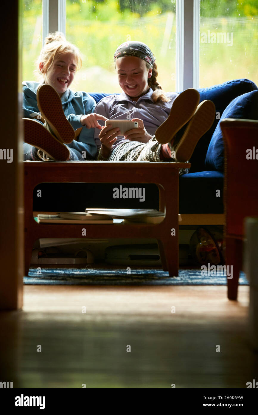 Teen girls laughing on a couch looking at something on a phone Stock Photo