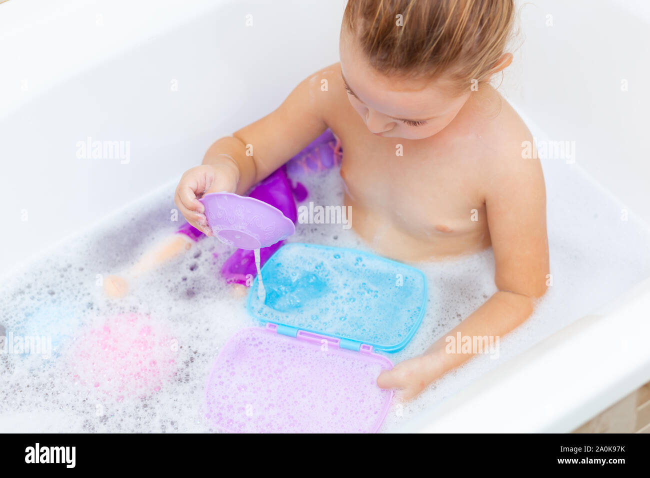 Cute adorable baby girl taking foamy bath in bathtub. Toddler playing