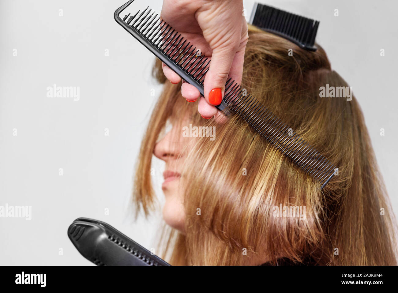 Professional hairdresser straightening long brown hair with hair irons in beauty salon. Close-up Stock Photo