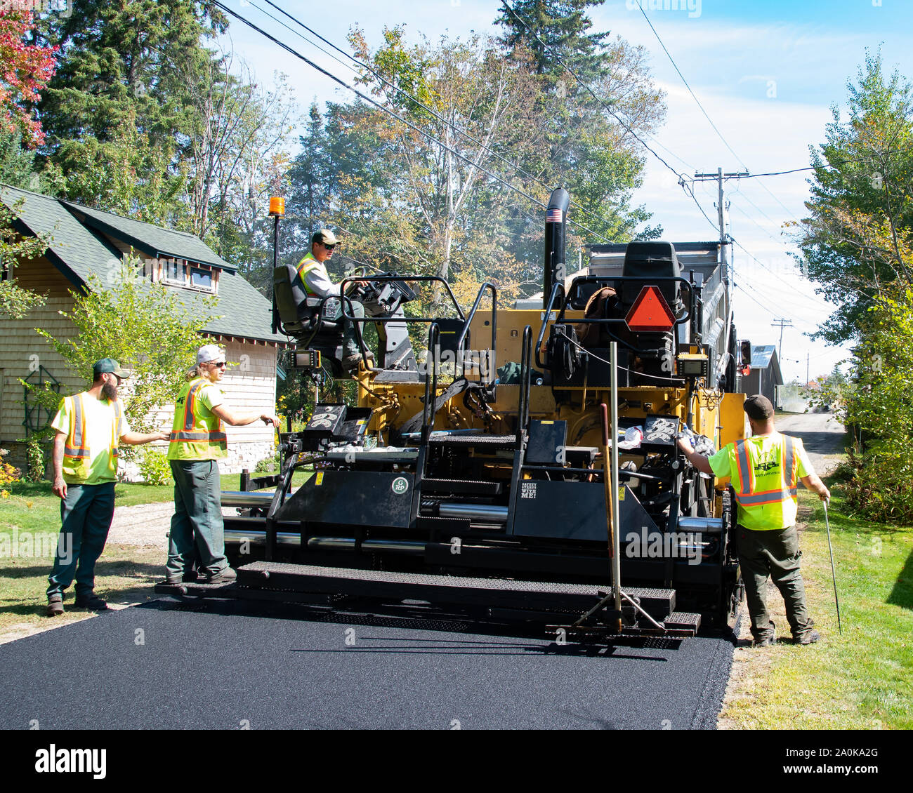 A dump truck and a paving machine laying new asphalt on a village street in Speculator, NY USA in early autumn Stock Photo