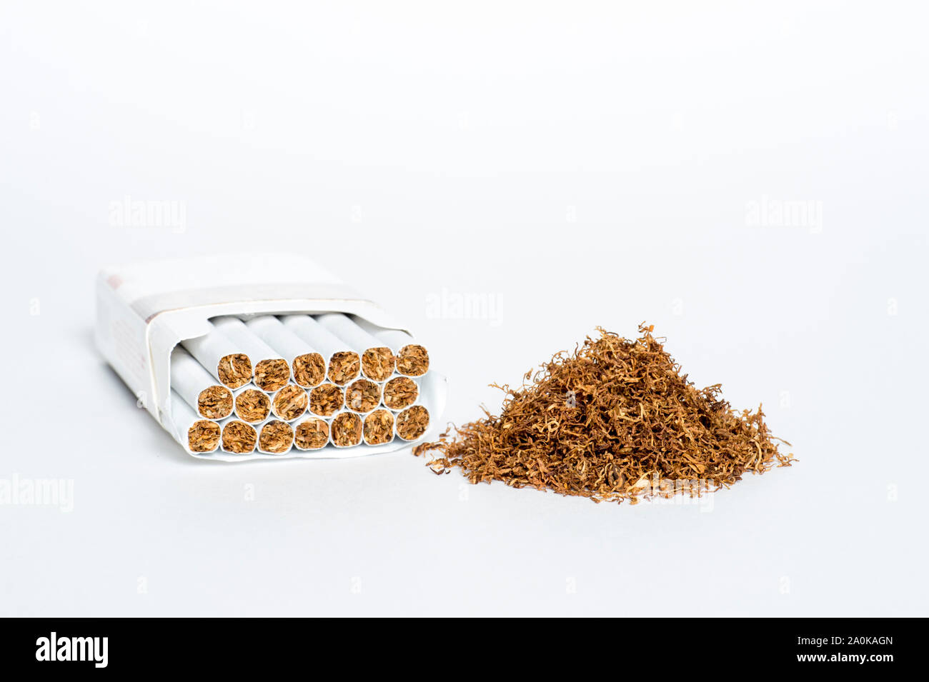 A pile of natural cigarette tobacco next to an open pack of cigarettes. The  concept of natural tobacco raw materials and additives of industrial produ  Stock Photo