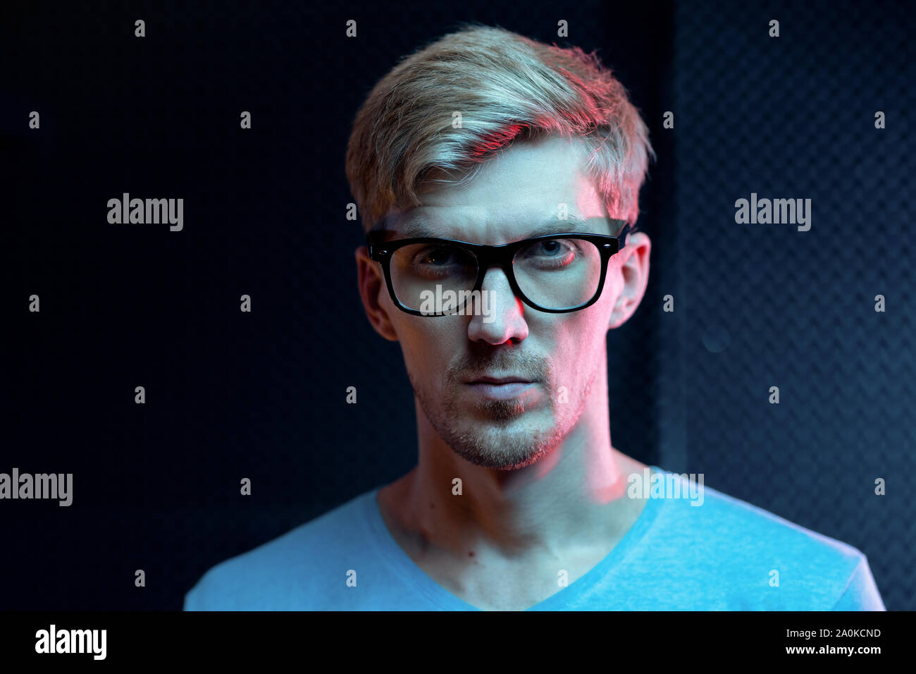 Serious young blond man of Caucasian ethnicity looking at you through eyeglasses Stock Photo
