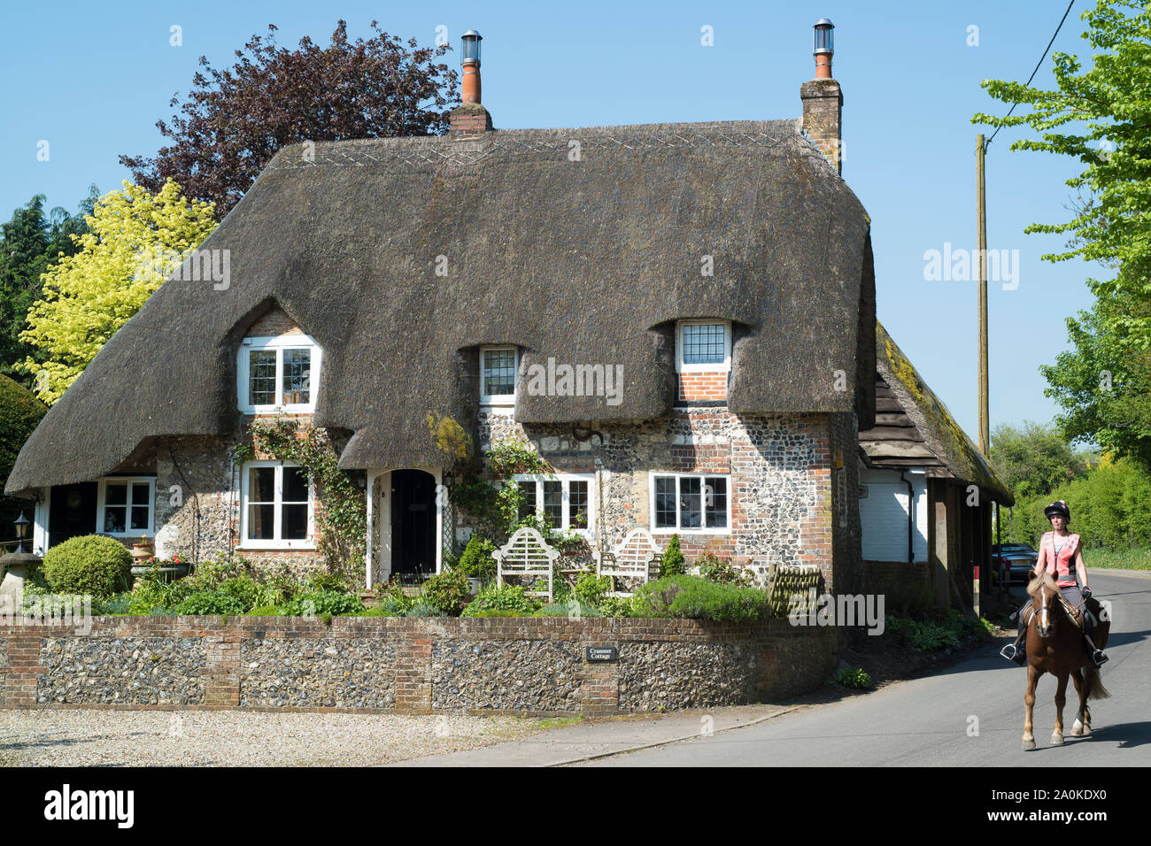 Horse rider passes typical English thatched cottage of brick and flint construction in Ramsbury, Wiltshire, UK Stock Photo