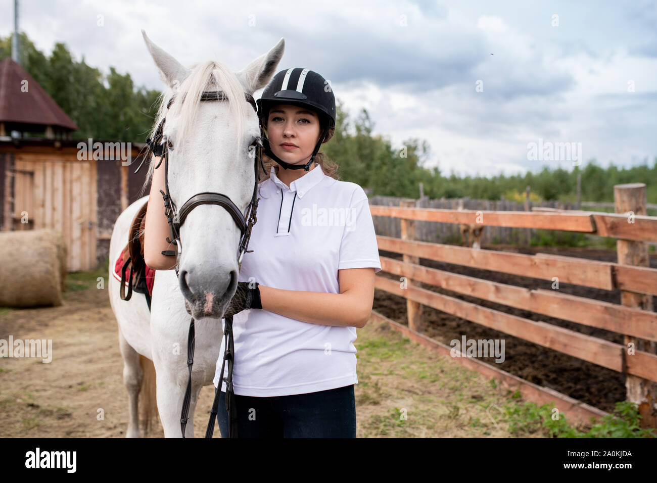 Young sportswoman in activewear standing by white purebred racehorse Stock Photo