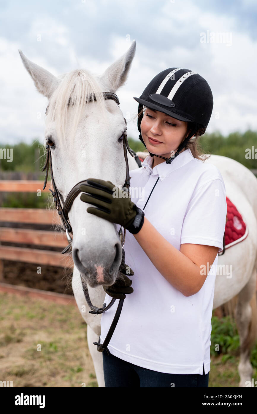 Young active female cuddling muzzle of white purebred racehorse Stock Photo