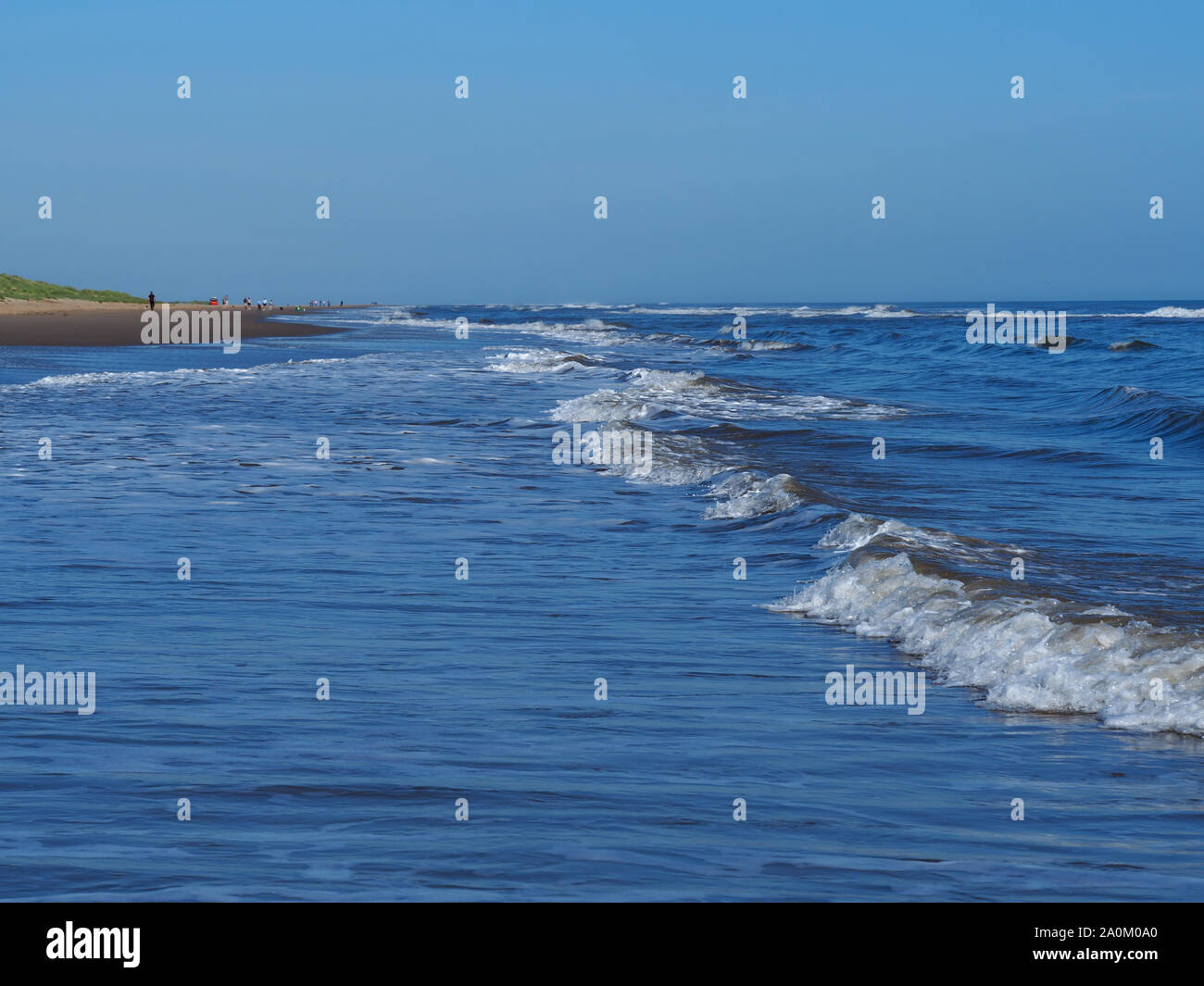 Gentle sea waves approaching the sandy beach at Mablethorpe, Lincolnshire, England, with a clear blue sky Stock Photo