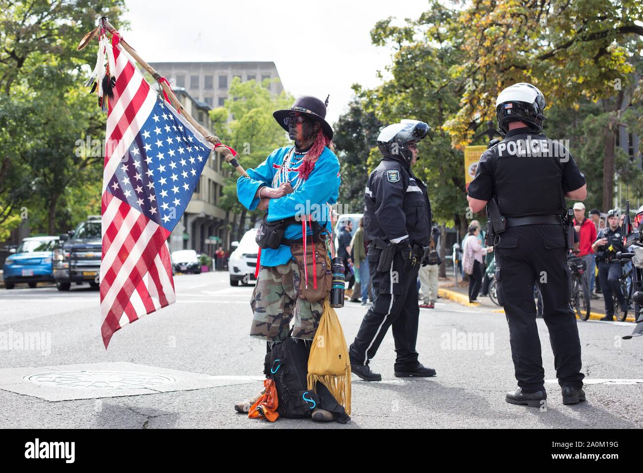 A native American man holding an upside down flag next to police at the Climate Strike rally in Eugene, Oregon, USA. Stock Photo