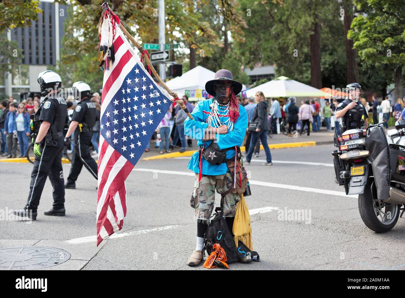 A native American man holding an upside down flag next to police at the Climate Strike rally in Eugene, Oregon, USA. Stock Photo
