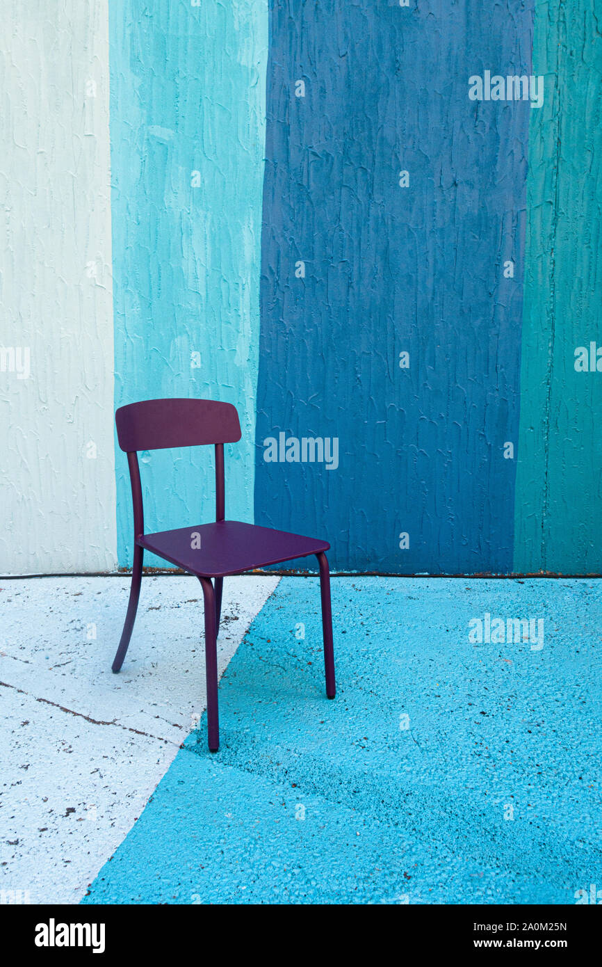 A solitary purple chair sitting on a background and floor of blue painted stripes Stock Photo