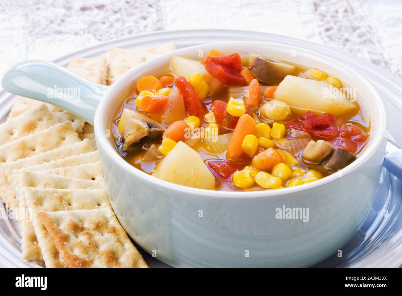 Warm homemade vegetable soup and served with crispy saltine crackers in a light blue colored bowl on a white plate. Stock Photo