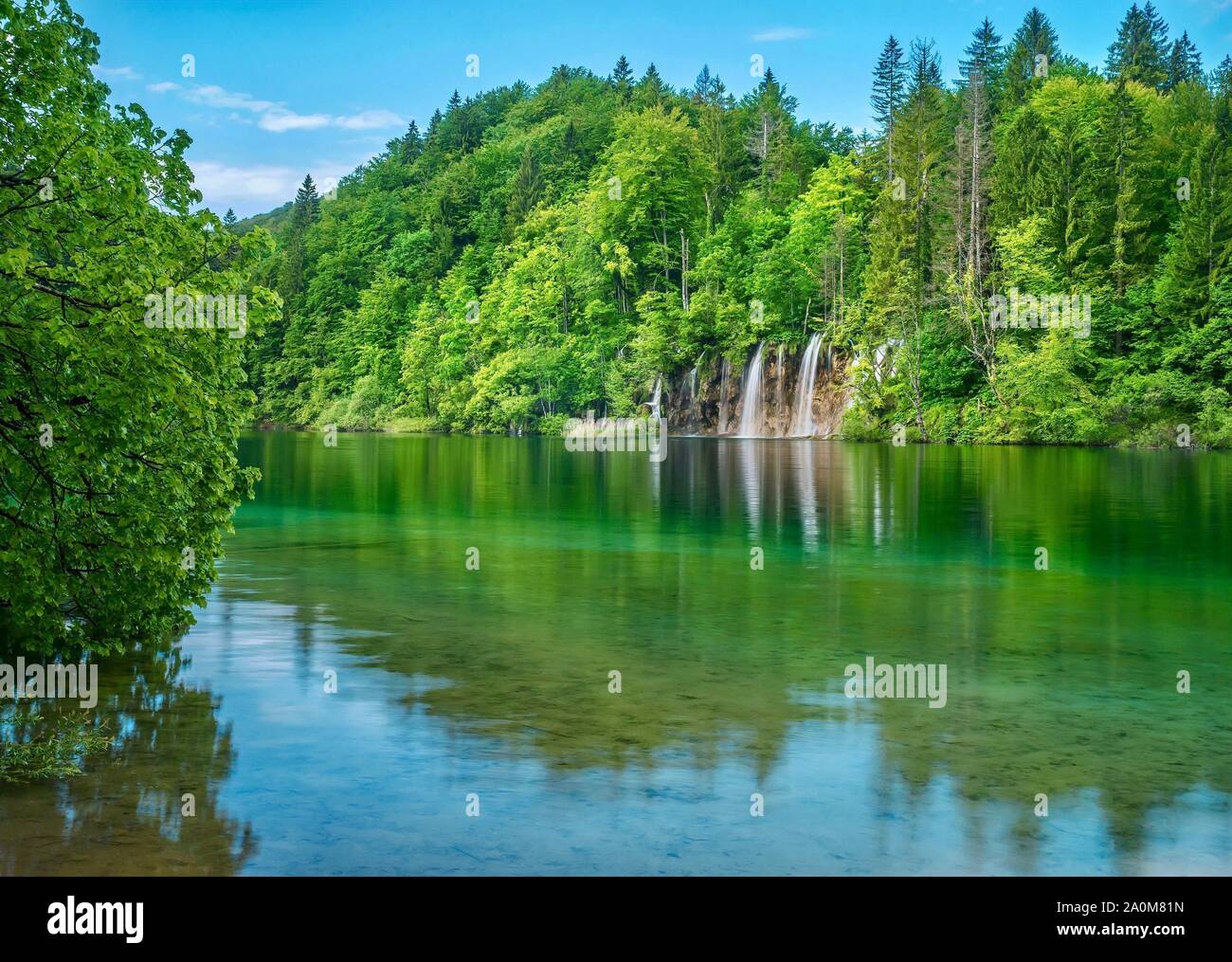 A beautiful, peaceful summer nature scene in the forest, with waterfalls and trees reflected in a calm lake. Plitvice Lakes National Park, Croatia. Stock Photo