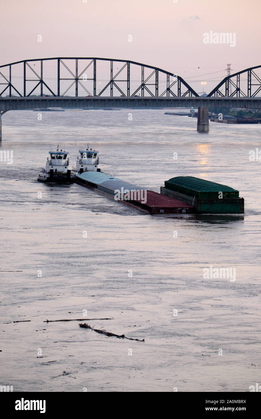 Tugboats fight their barges upriver against a strong current on the Mississippi River at St. Louis, MO near dusk. Stock Photo