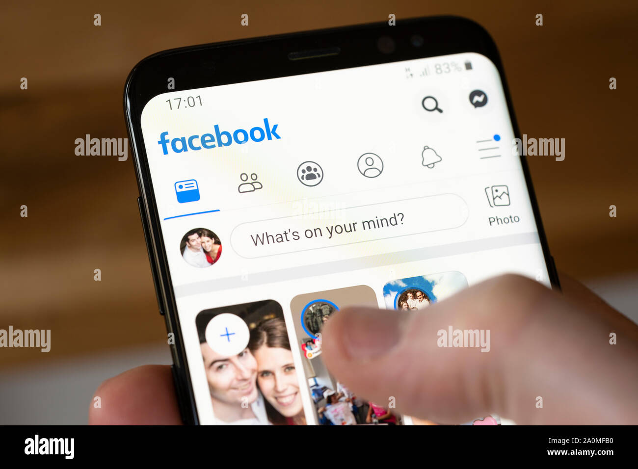 A man holding a smartphone showing the Facebook app and logo Stock Photo