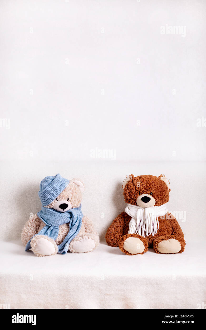 Children's toys teddy bears sitting on a white sofa in a knitted white and blue scarf and hat. Selective focus. Stock Photo