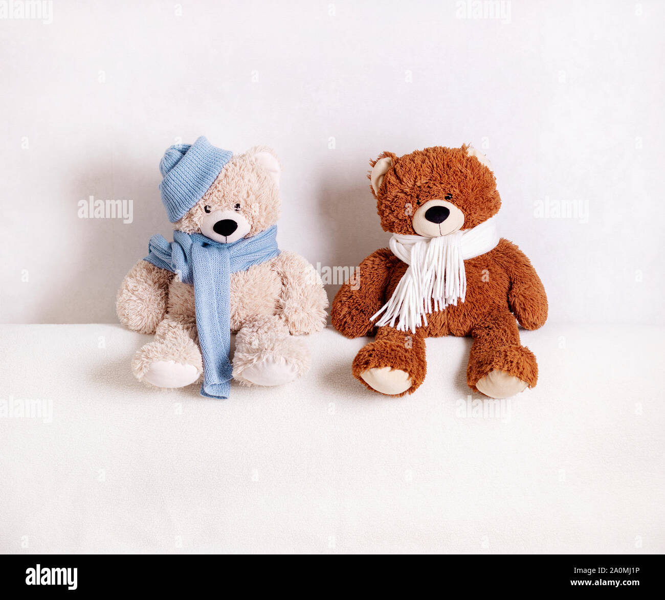 Children's toys teddy bears sitting on a white sofa in a knitted white and blue scarf and hat. Selective focus. Stock Photo